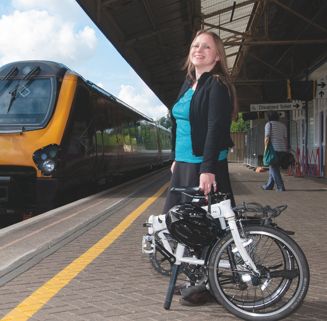 Lady standing on a station platform waiting for the train, holding a folding bike